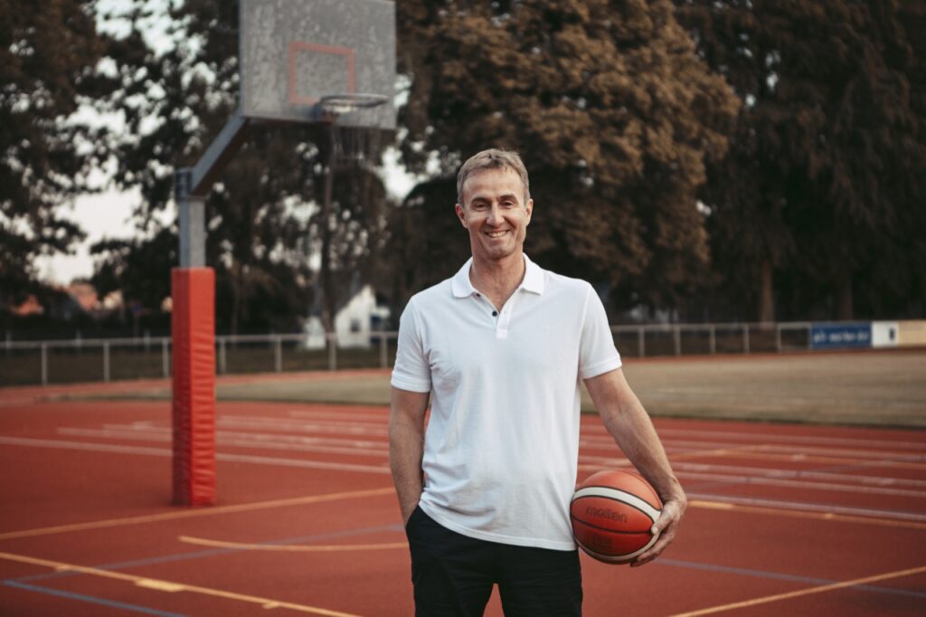 peter kwapil, der headcoach von provictus, steht vor einem basketballkorb und hält einen basketball.