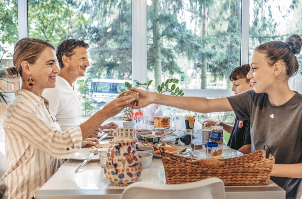 Balance zwischen Familie und Leistungssport finden, Familie die gemeinsam frühstückt im hellen Esszimmer mit Blick ins Grüne