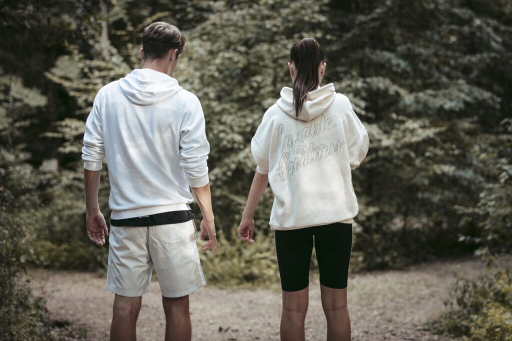 junge sportler:innen in hellen hoodies von hinten auf einem waldweg, motivation im sport