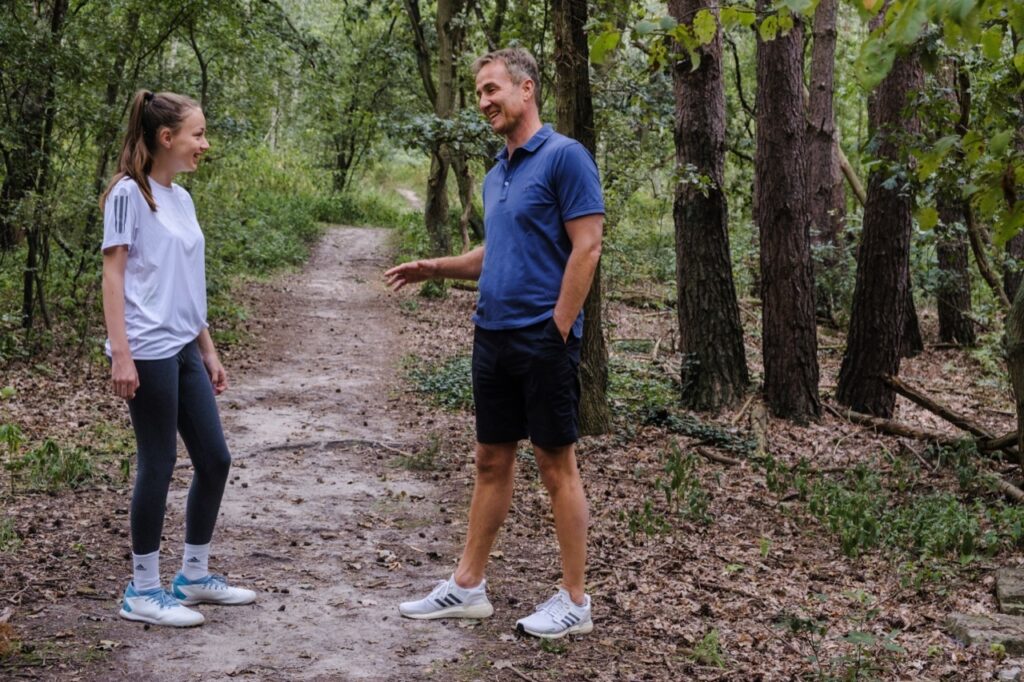 junge sportlerin und coach im gespräch auf waldweg – selbstvertrauen im sport aufbauen