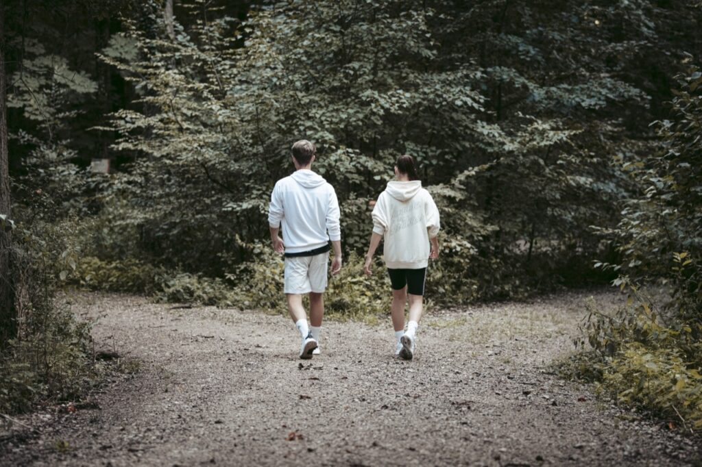 zwei junge sportler:innen gehen einen waldweg entlang, symbolbild für selbstbewusstsein stärkende übungen